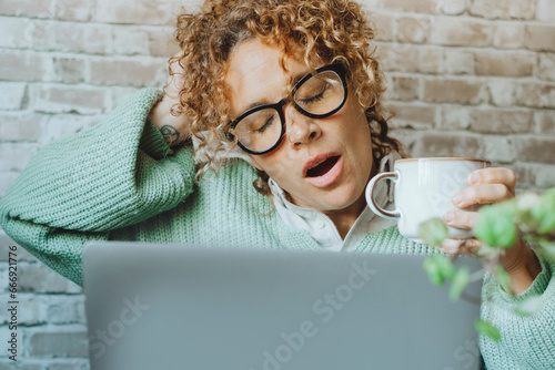 Tired woman suffering insomnia working in front of. a laptop computer and drinking coffee for caffeine. Concept of overwork condition. Home office job business genale people doing yawn alone. Online