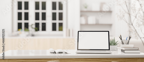 A white-screen laptop mockup and accessories on a white tabletop in a modern, white living room.