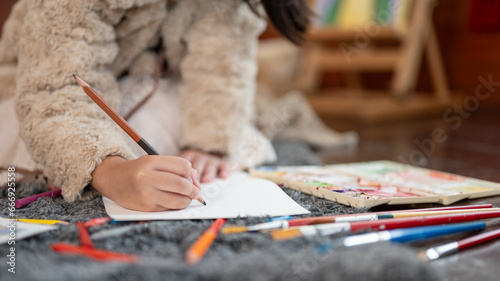 Close-up image of a young girl holding a pencil color and drawing or coloring on paper. Kid leisure