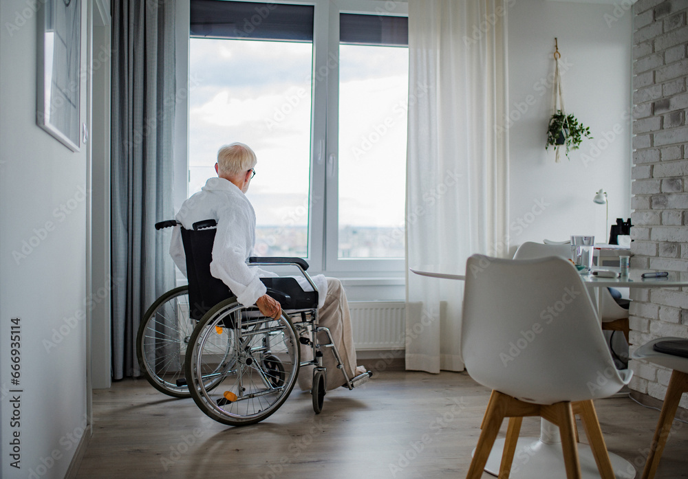 Senior man in a wheelchair spending time alone in apartment. Concept of loneliness and dependence of retired people. - obrazy, fototapety, plakaty 