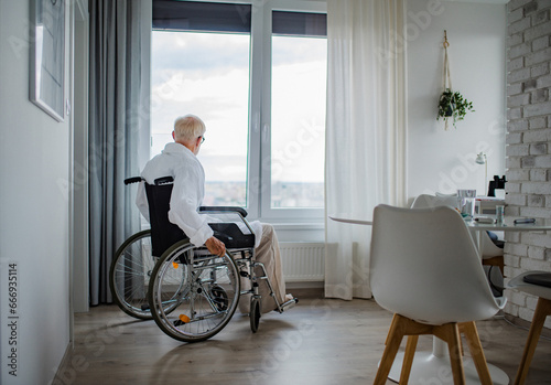 Senior man in a wheelchair spending time alone in apartment. Concept of loneliness and dependence of retired people.