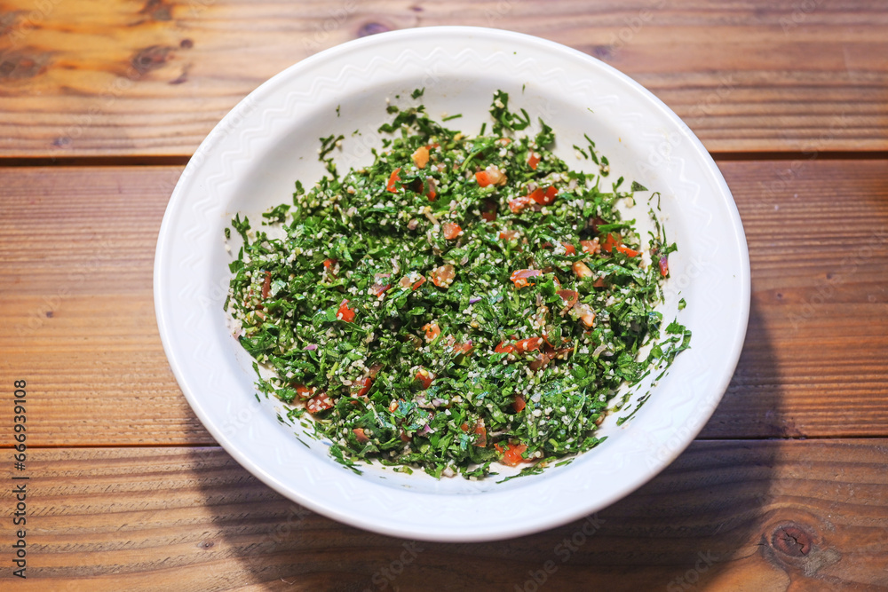 Taboule, Lebanese parsley salad with tomatoes, onions and mint in a white bowl on a rustic wooden table, seen from above, copy space, selected focus Taboule, Lebanese parsley salad with tomatoes, onions and mint in a white bowl on a rustic wooden table, seen from above, copy space, selected focus