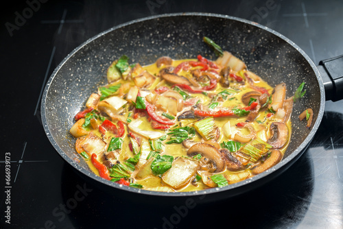 Vegetable Thai curry in a frying pan, ingredients like red bell pepper, mushroom, pak choi, seasoned with ginger, turmeric and onions, cooked in coconut milk, selected focus