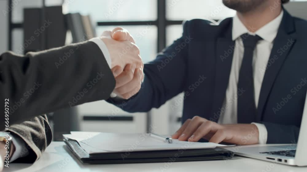 Cropped slowmo shot of unrecognizable businessman signing document and handshaking with business partner after closing successful deal in office