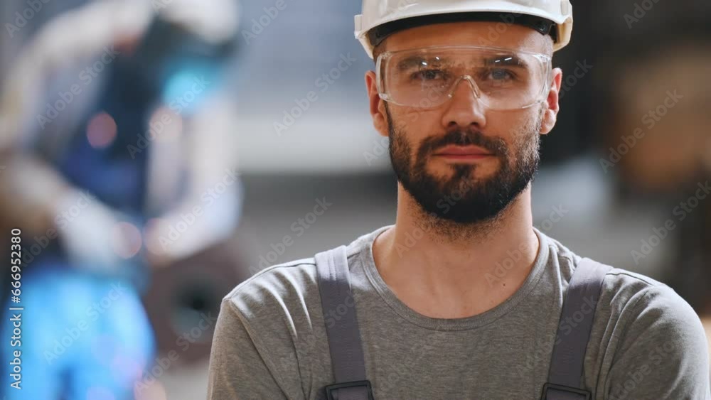 Portrait of a professional heavy industry engineer. Worker wearing protective uniform, goggles and helmet, smiling. In the background is a disoriented large industrial plant where welding sparks fly. Portrait of a professional heavy industry engineer. Worker wearing protective uniform, goggles and helmet, smiling. In the background is a disoriented large industrial plant where welding sparks fly.
