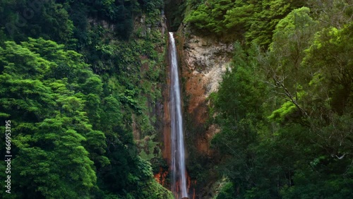 Cinematic Aerial Drone shot of Ribeira Quente natural waterfall in Sao Miguel in the Azores - Portugal.
View of lush green tropical forest surrounding the waterfall.
Camera moving forward rising up. photo