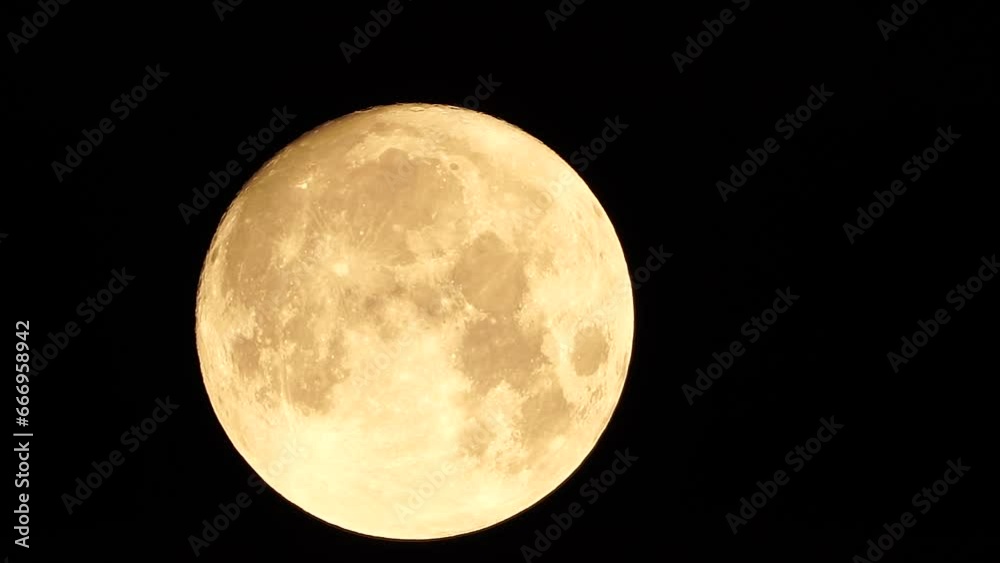 A glowing golden huge full moon seen from earth through the atmosphere against a starry night sky. A large full moon moves across the sky, the moon moving from the left frame to the right. A glowing golden huge full moon seen from earth through the atmosphere against a starry night sky. A large full moon moves across the sky, the moon moving from the left frame to the right.