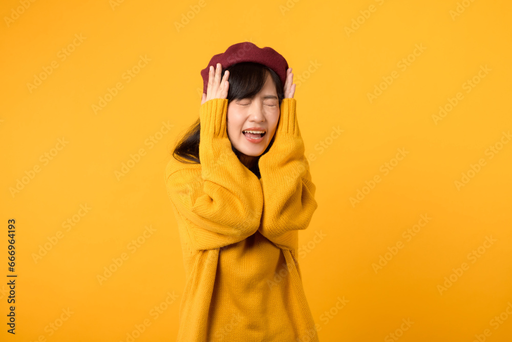 Amidst the noise, a stylish Asian lady, dressed in a yellow sweater and red beret, listens attentively against a vibrant yellow setting. Amidst the noise, a stylish Asian lady, dressed in a yellow sweater and red beret, listens attentively against a vibrant yellow setting.