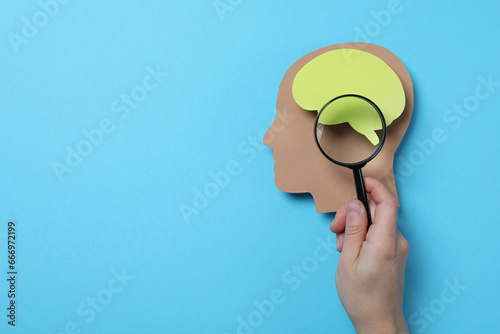 Magnifying glass in hand and paper head on blue background, space for text photo