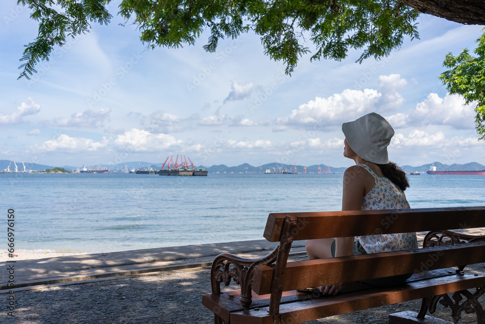 Rear View of Woman Sitting on Bench Looking at Ocean in Summer