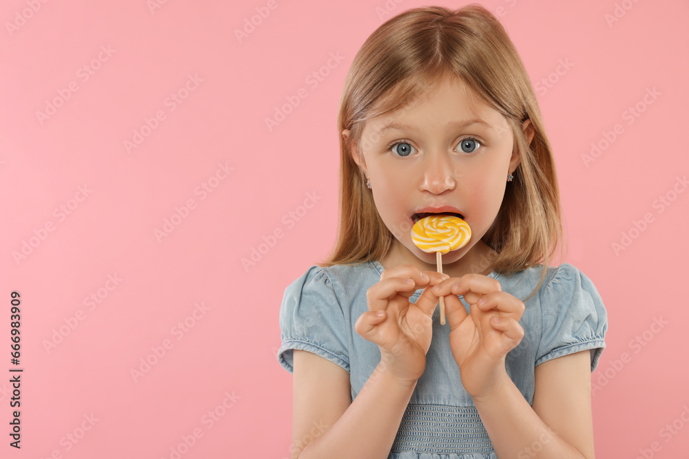 Portrait of cute girl licking lollipop on pink background, space for text Portrait of cute girl licking lollipop on pink background, space for text