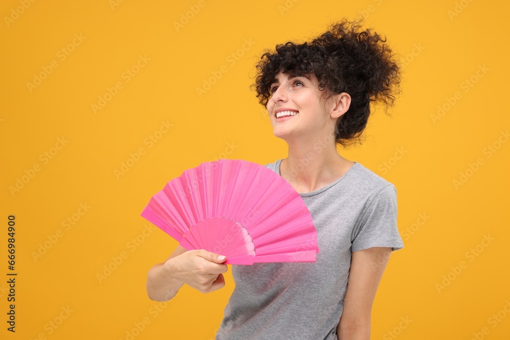 Happy woman holding hand fan on orange background. Space for text Happy woman holding hand fan on orange background. Space for text