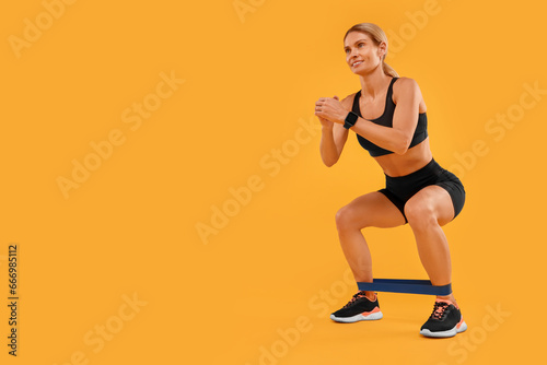 Fototapeta Naklejka Na Ścianę i Meble -  Woman exercising with elastic resistance band on orange background, low angle view. Space for text