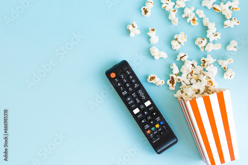 TV remote and popcorn on a blue background. TV watching concept with copy space. Movie night. Entertainment concept.