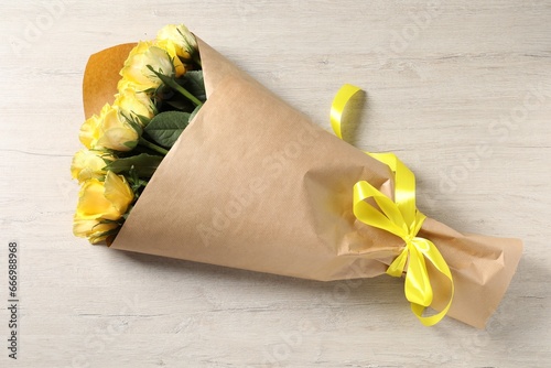 Beautiful bouquet of yellow roses with ribbon on wooden table, top view