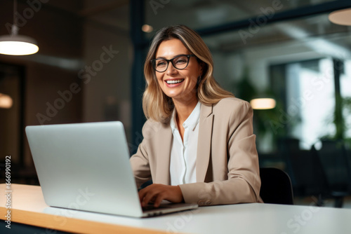 Happy mid aged business woman working on laptop in office. hr manager communicating by conference call, remote online job interview on laptop