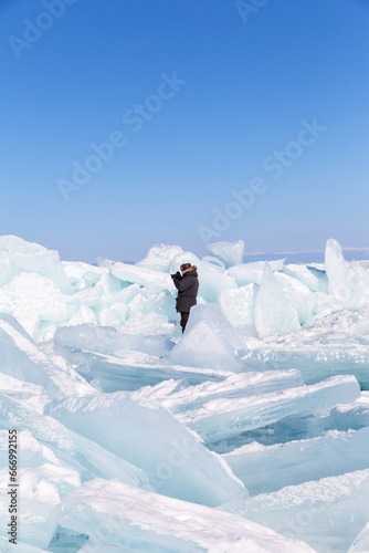 Baikal Lake on sunny cold February day. Tourist in warm clothes photographed ice hummocks with large pile of blue transparent ice floes on  frozen Small Sea. Unusual landscape. Natural background