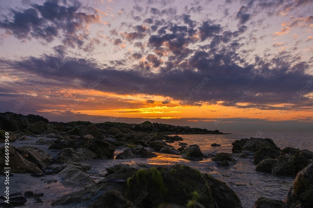 Stunning coastal sunrise scene with a rocky shoreline lined with lush green moss