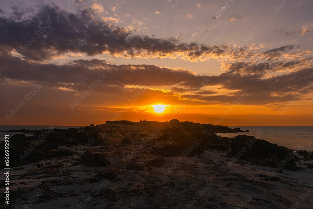 Breathtaking view of a golden sunset over the horizon, seen from the rocky shoreline