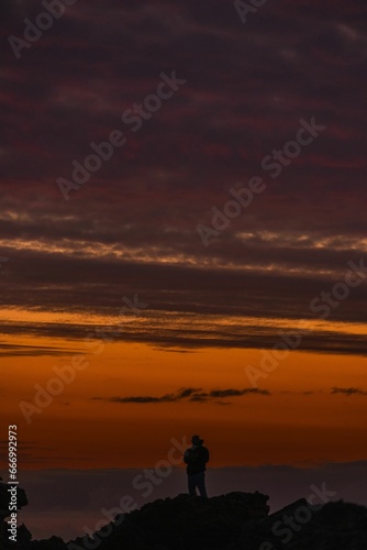 a silhouetted person robes standing on a rocky outcrop at sunset