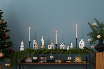 Aesthetic composition of christmas living room interior with wooden console, spruce, white candles, christmas tree with balls, gifts, blue wall, wreath and personal accessories. Home decor. Template.