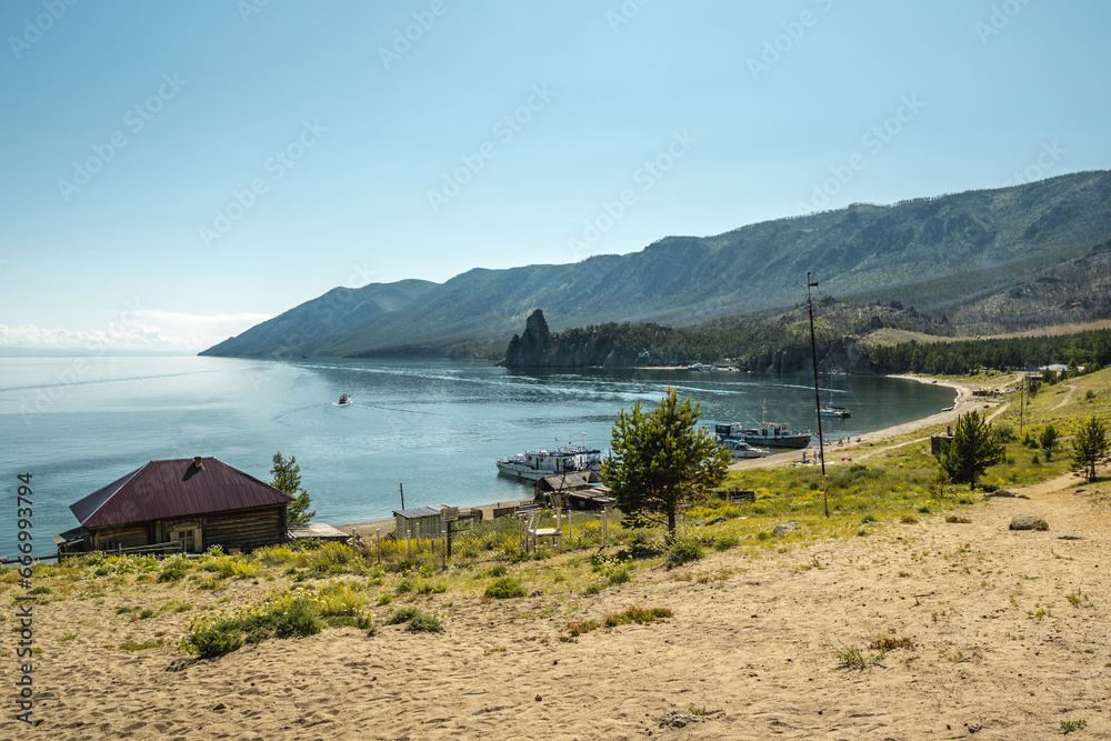 Sandy shore of summer Lake Baikal. Coniferous trees with large roots cover the shore. Tourism and the unique nature of Lake Baikal