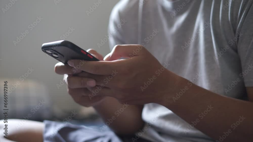 Hands of Asian man holding checking touching scrolling smartphone from bed room Hands of Asian man holding checking touching scrolling smartphone from bed room
