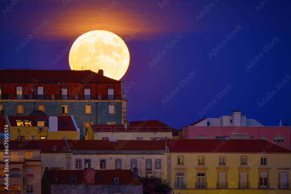 Big full moon rising over old houses in European city, close up, night