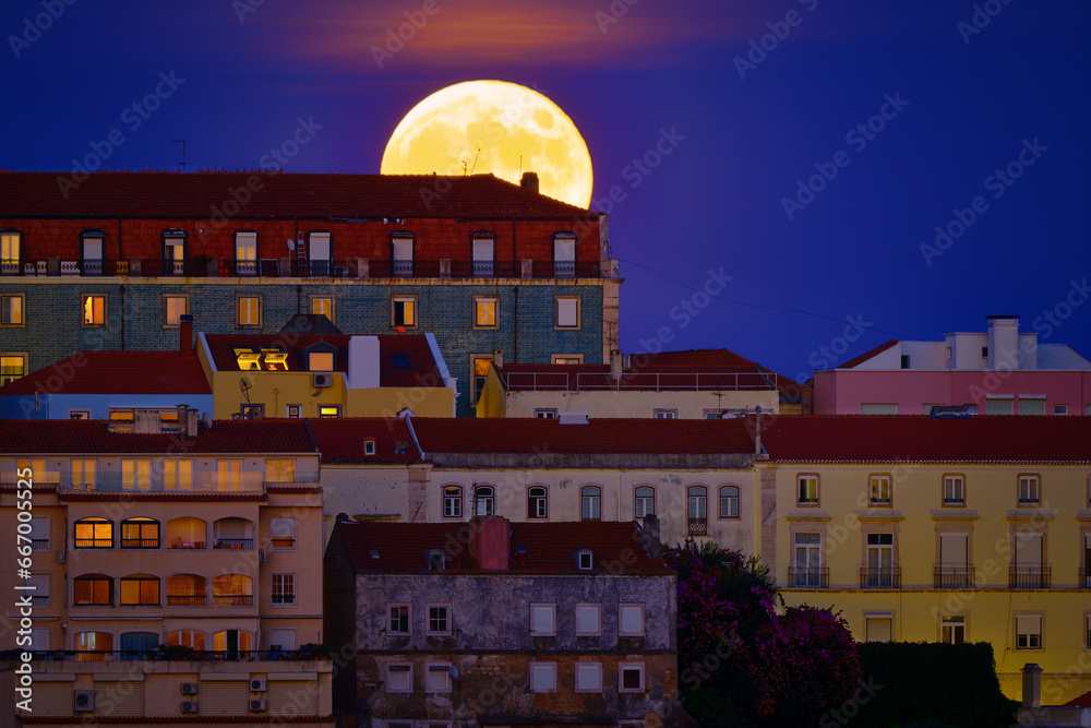 Big full moon rising over old houses in European city, close up, night