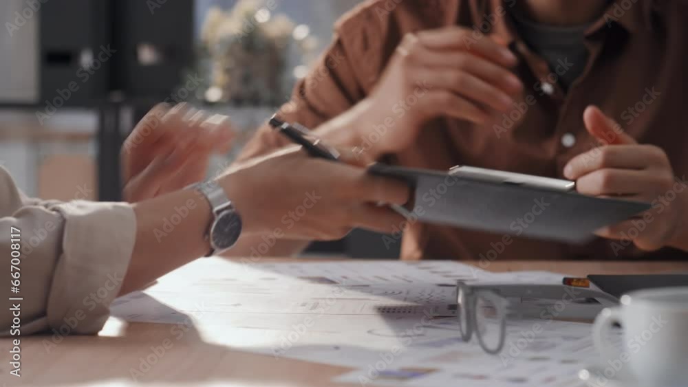 Medium pan shot of two unrecognisable business partners in casual wear signing contract using clipboard and then handshaking in office Medium pan shot of two unrecognisable business partners in casual wear signing contract using clipboard and then handshaking in office