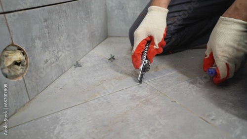 A man uses a trowel to remove old mortar. The concept of laying ceramic tiles in the bathroom. A worker cleans the seams on the floor after laying tiles. Cleaning grout lines on ceramic tile floors. photo