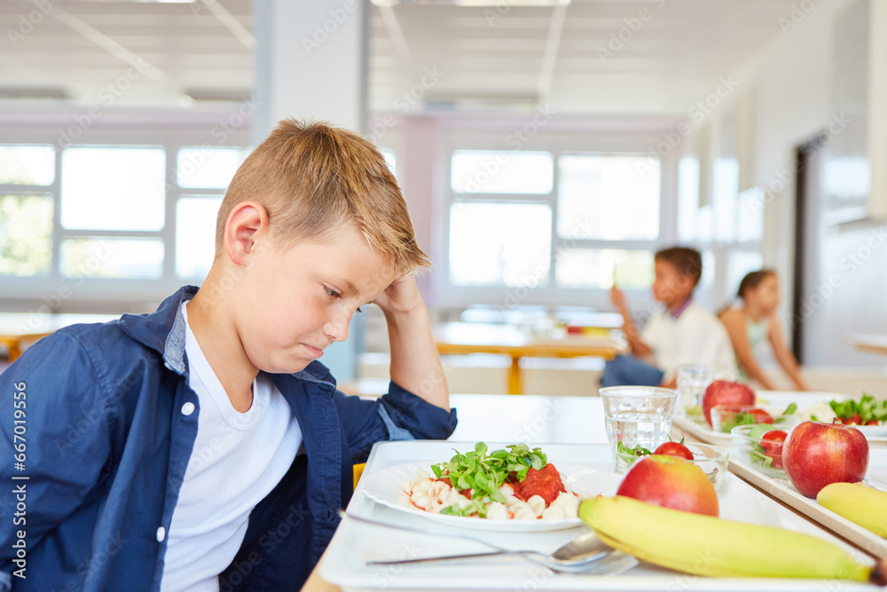 Sad schoolboy staring at food plate in cafeteria Sad schoolboy staring at food plate in cafeteria
