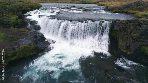 Aerial: Reykjafoss waterfall presents itself as a powerful cascade of water.  It is a hidden gem amidst Iceland's enchanting landscapes. Framed by moss-covered rocks and vibrant, verdant vegetation. photo