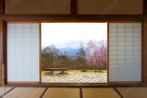 A view of the spring mountains and a bench looking through the door of a traditional Japanese house.