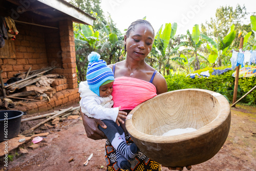 Portrait of a beautiful young African mother holding her baby and looking a the mortar with flour photo