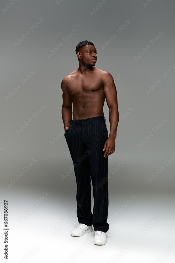sportive african american man with strong body and hand in pocket looking away on grey, full length