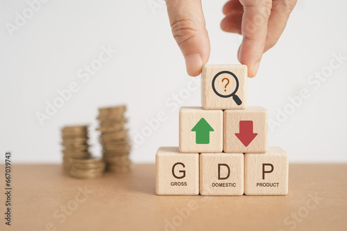 For global economy GDP text, gross domestic product , on stack of wooden cube block with up and down arrow  and blurred coins photo