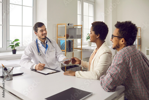 Happy black married couple visiting and consulting with family doctor. General practitioner gives therapy prescription to patients. Healthy young husband and wife get good health exam analysis results