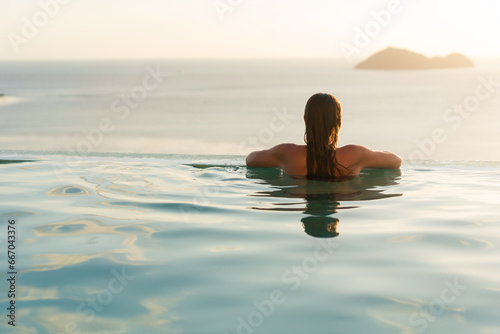 Girl in the pool among tropical palms and mountains at sunset