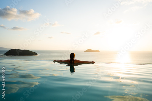 Girl in the pool among tropical palms and mountains at sunset