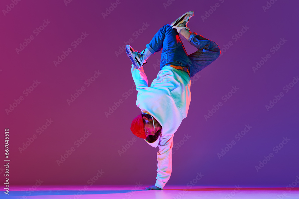 Man in stylish sportswear in motion, dancing breakdance isolated over gradient studio background in neon light. Concept of contemporary dance, street style, fashion, hobby, youth. Ad - obrazy, fototapety, plakaty 
