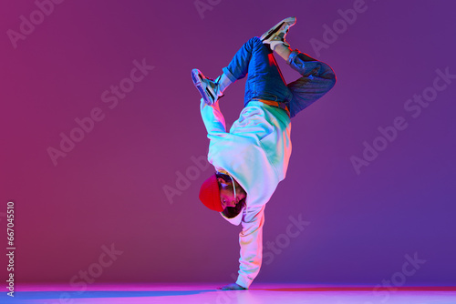 Man in stylish sportswear in motion, dancing breakdance isolated over gradient studio background in neon light. Concept of contemporary dance, street style, fashion, hobby, youth. Ad