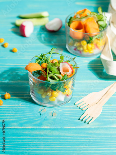 A bowl with fresh vegetables and micro greenery on a blue wooden background with eco-friendly cutlery. Blurred background.