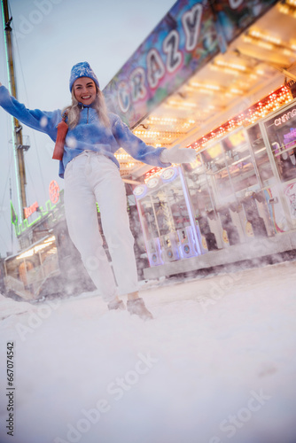 Cheerful and stylish woman, dressed in warm clothes, is having fun in a snowy winter amusement park