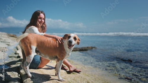 Woman relax with her dogs sitting on ocean coast beach. Young brunette petting the back of red funny pet. Spending time together with best friends. © Anastasia Pro