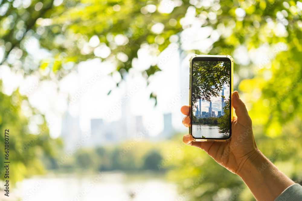 A person takes a mobile photo of the New York City's skyline seen through the trees of Central Park in New York, USA.