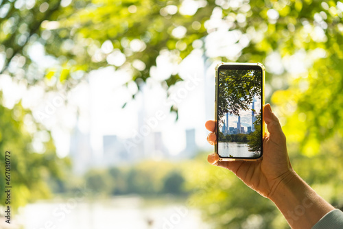 Obraz na płótnie A person takes a mobile photo of the New York City's skyline seen through the trees of Central Park in New York, USA. w salonie