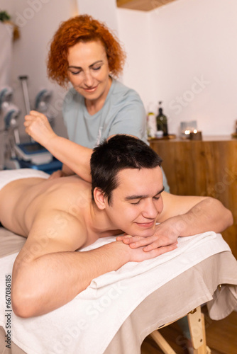 Closeup of handsome man having full body massage at male spa. Unrecognizable female therapist rubbing middle aged man shoulders, making relaxing massage. Spa, massage, cosmetology for men