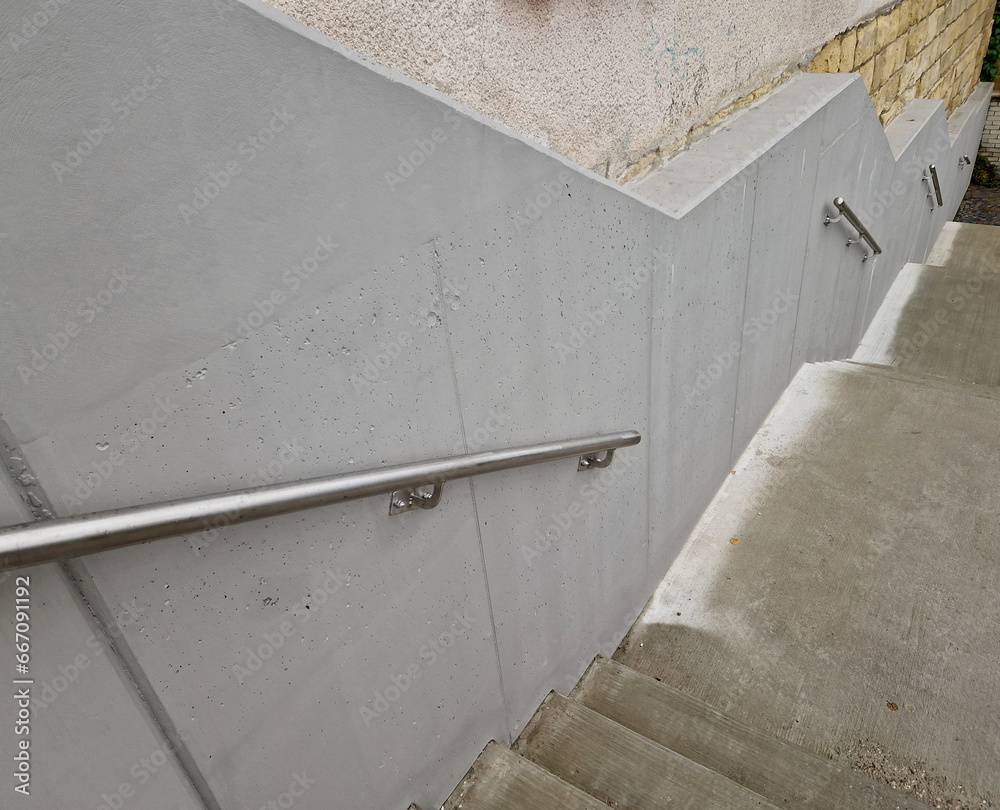 Obraz premium a staircase with concrete sides at a public building. the safe staircase has two handrails, one with a reduced height for children under 12 at the entrance to the school, brick, black, red. forgery
