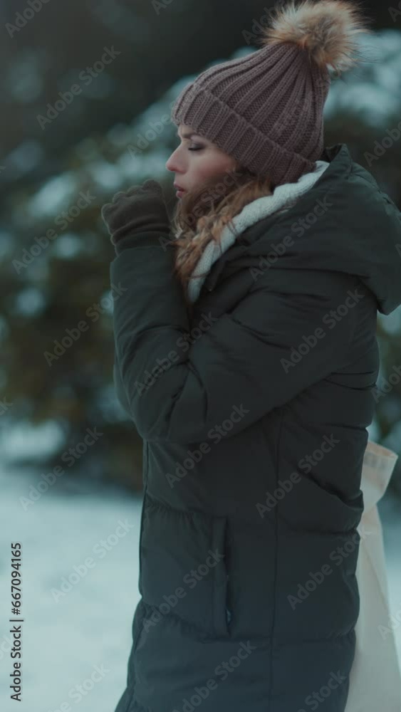 unhappy modern woman in green coat and brown hat outdoors in the city park in winter with mittens and beanie hat coughing. unhappy modern woman in green coat and brown hat outdoors in the city park in winter with mittens and beanie hat coughing.